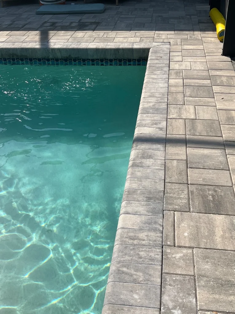 Close-up of pool edge coping with gray concrete pavers and turquoise water