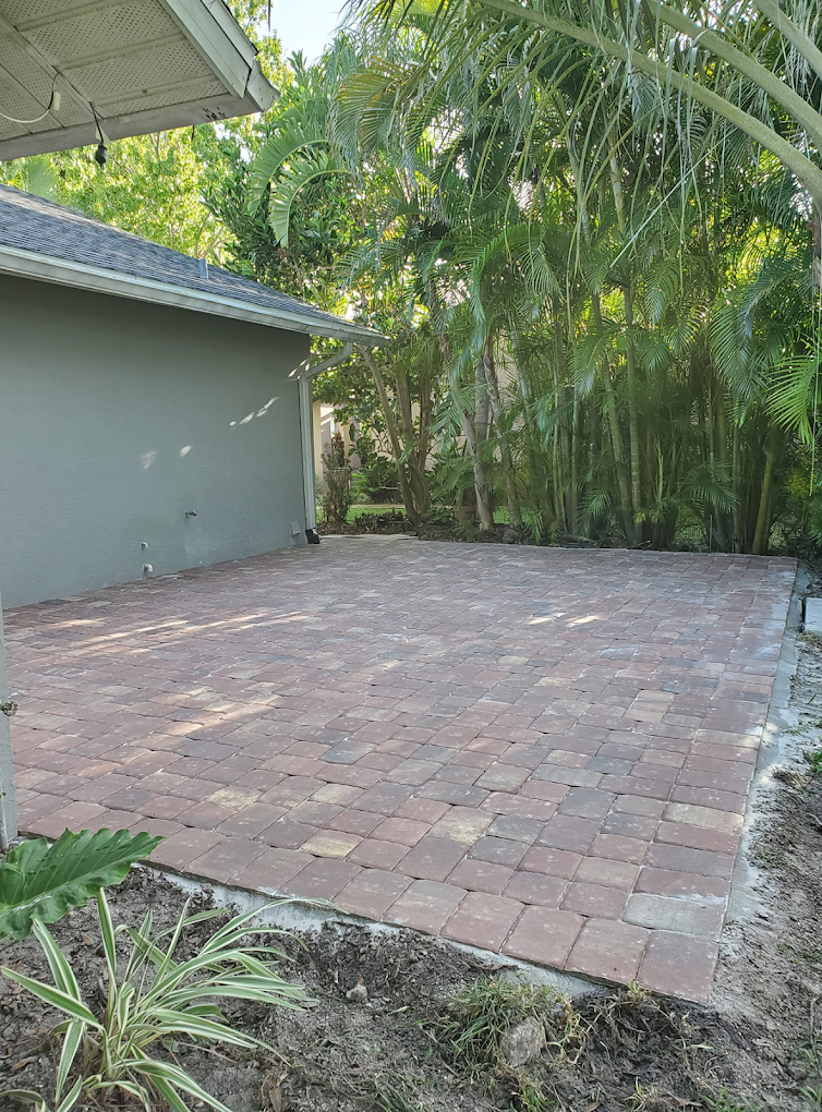 Fresh red brick paver patio installation with tropical landscaping backdrop