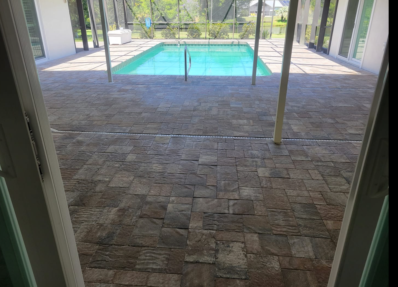 Wide-angle lanai and pool deck paver installation with screened enclosure in Florida home