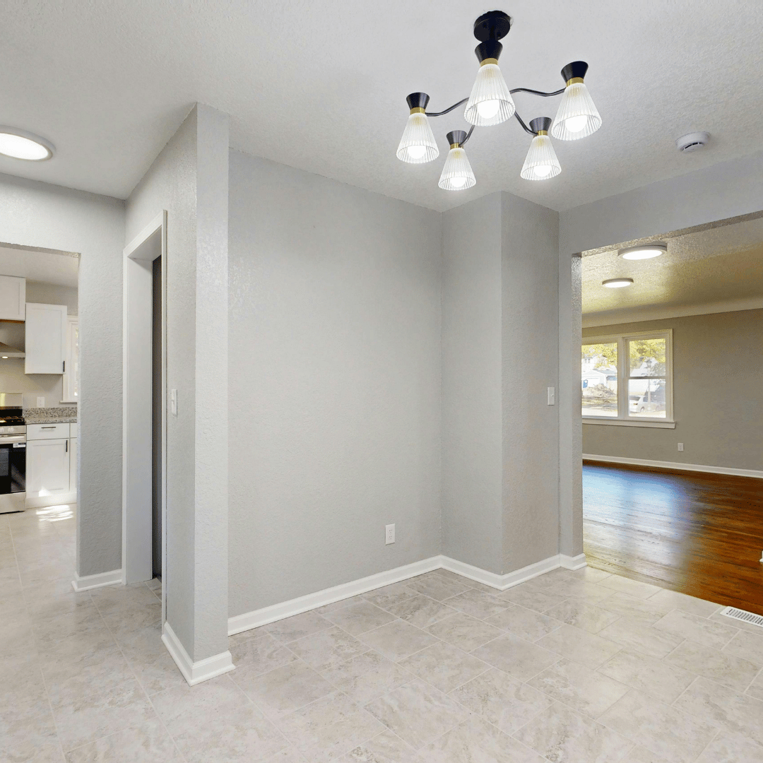 Finished basement with light tile flooring, gray walls, modern chandelier, and view into kitchen area