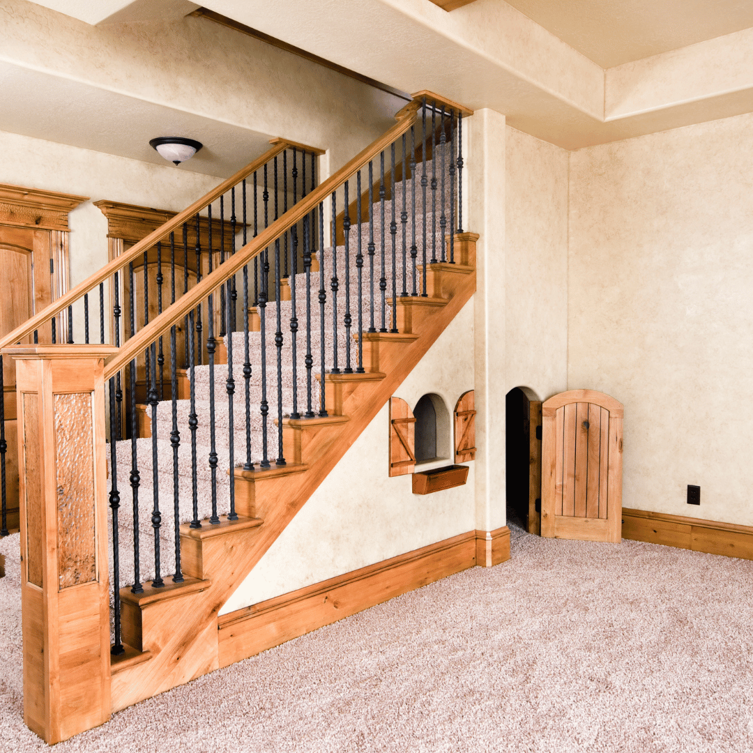 Custom oak staircase with black iron balusters leading to finished basement, featuring built-in pet door under stairs
