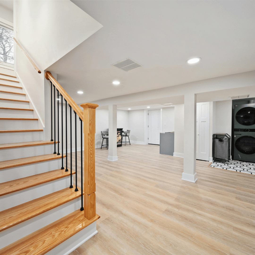 Bright open-concept finished basement with light wood flooring, oak stair railing, laundry area, and bar seating nook