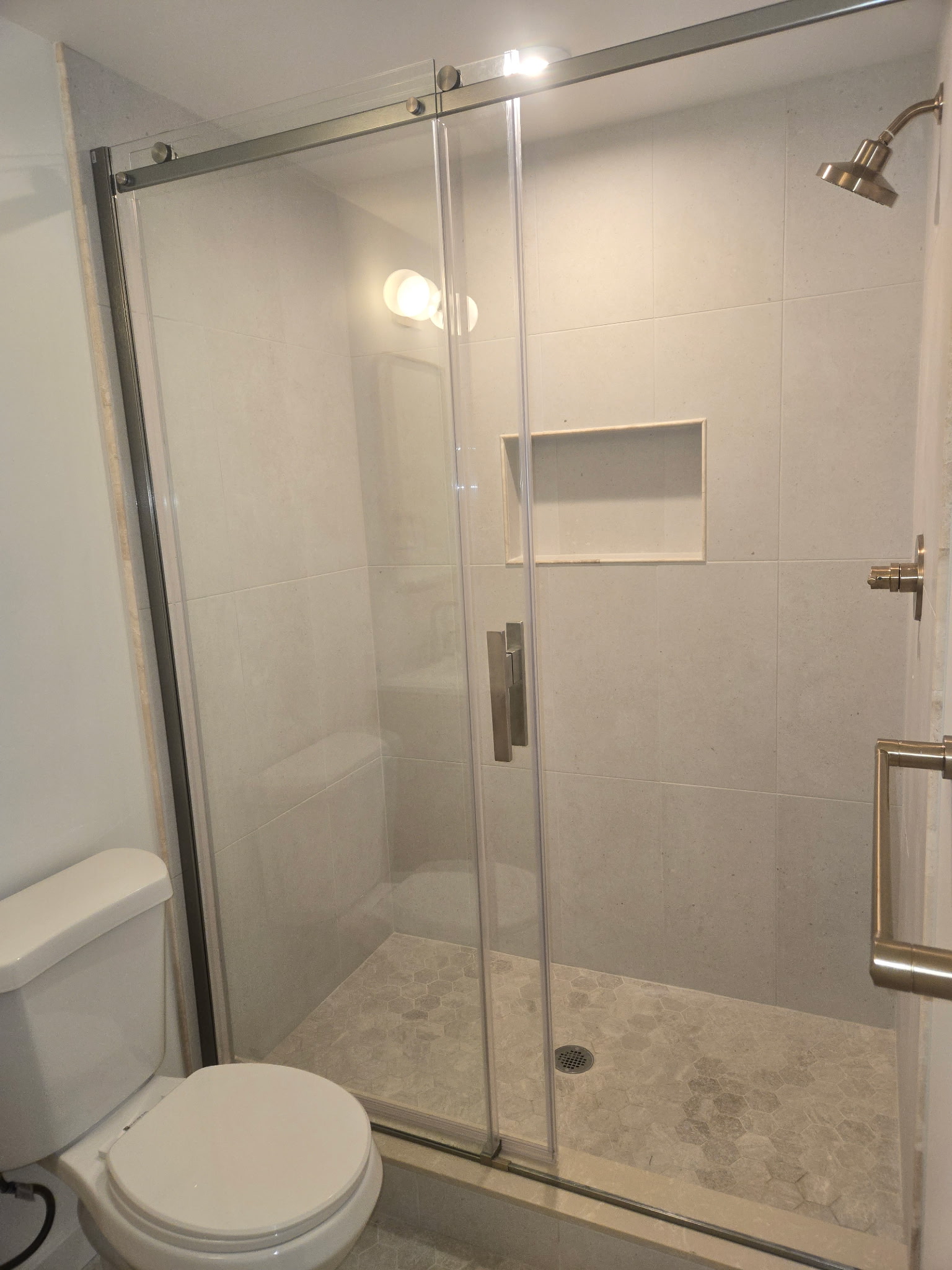 Frameless glass shower enclosure with hexagon tile floor, brushed nickel fixtures, built-in niche, and safety grab bar