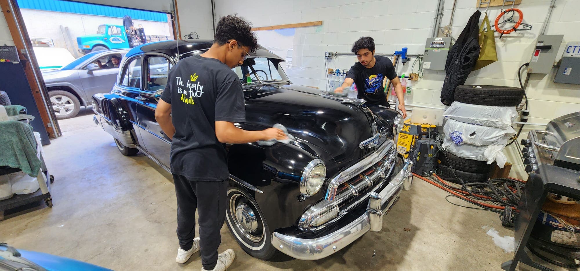 Students performing hands-on detailing on a classic black vehicle in the shop