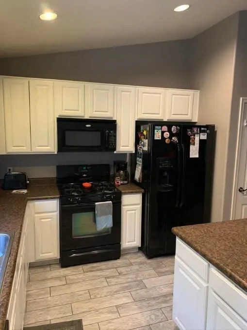 Cream painted kitchen cabinets with black appliances and brown granite countertops