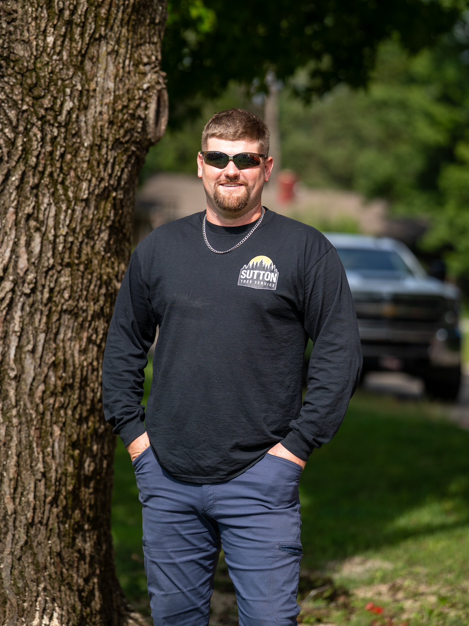 Sutton Tree Service owner in Sutton Tree Service shirt standing by tree