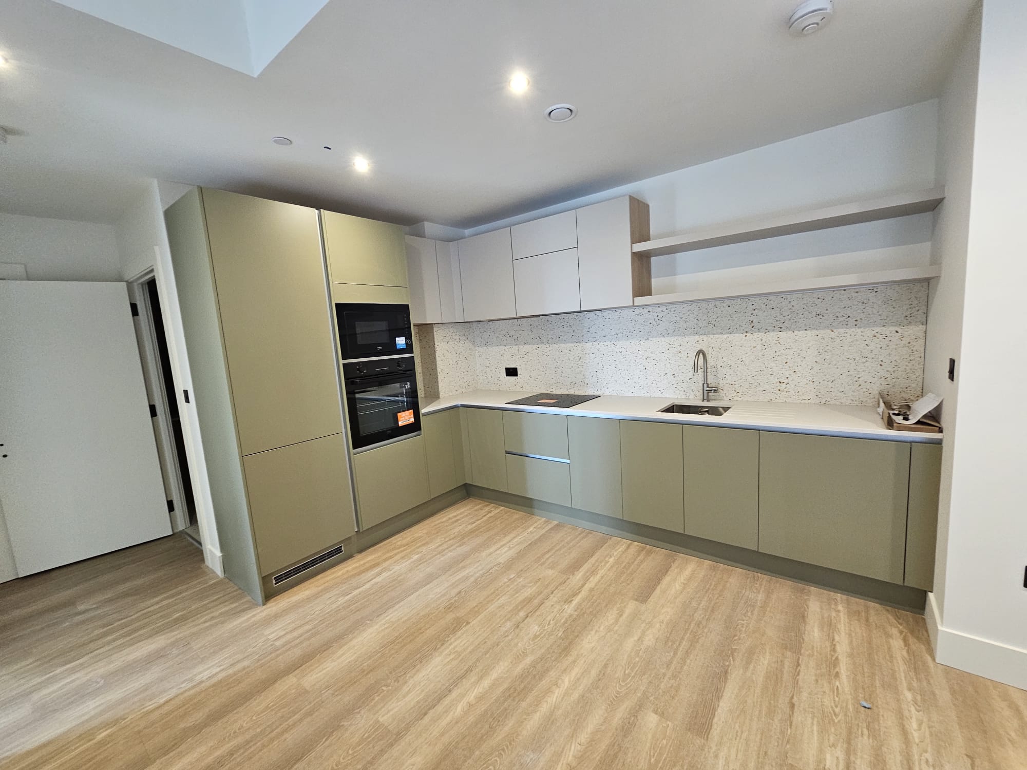 Wide-angle view of completed modern apartment kitchen installation with engineered wood flooring in Surrey Quays