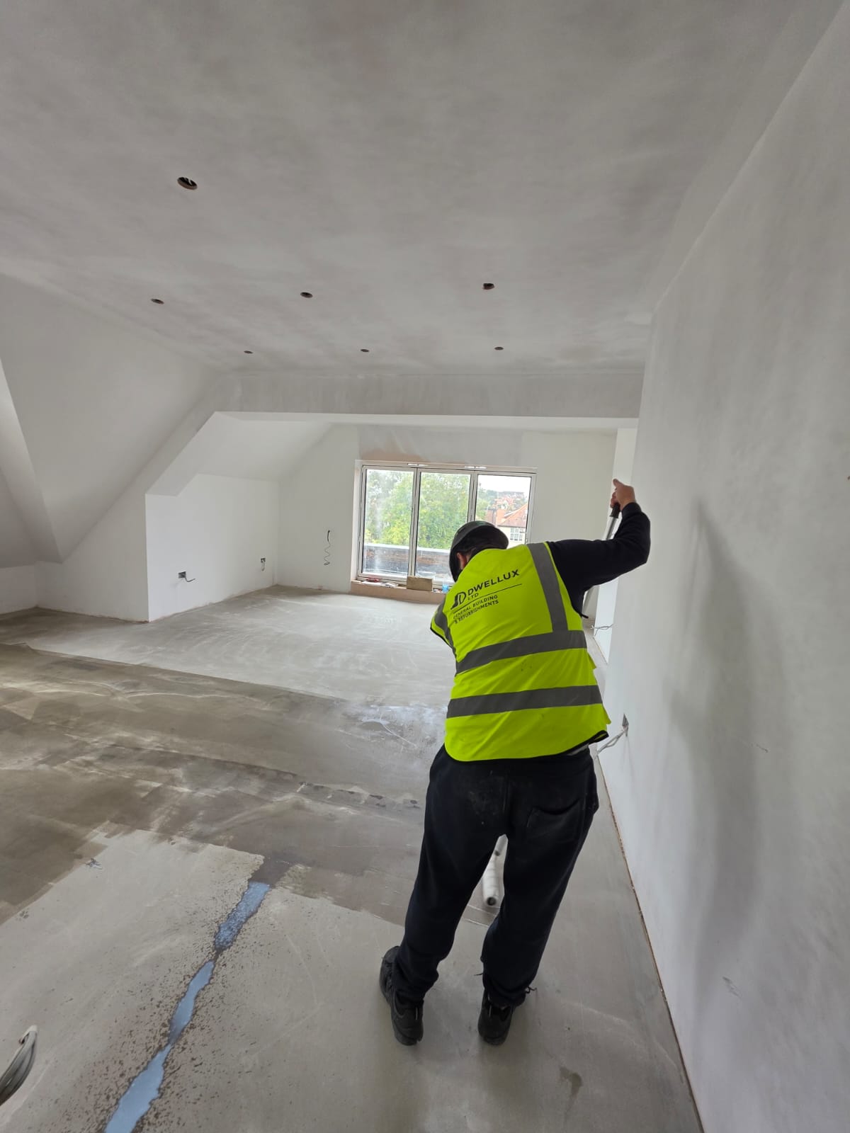 DWELLUX tradesman in high-vis vest applying surface primer to walls and floor in dormer room in Southend-on-Sea