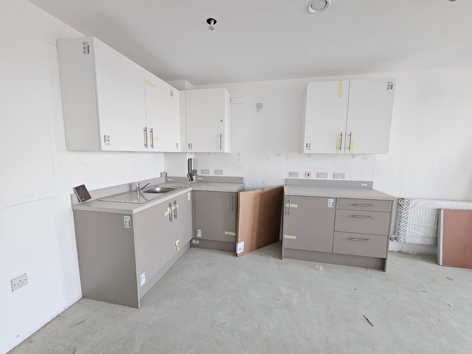 Social housing kitchen unit installation in progress with protective tape and precision cabinet fitting in Surrey Quays