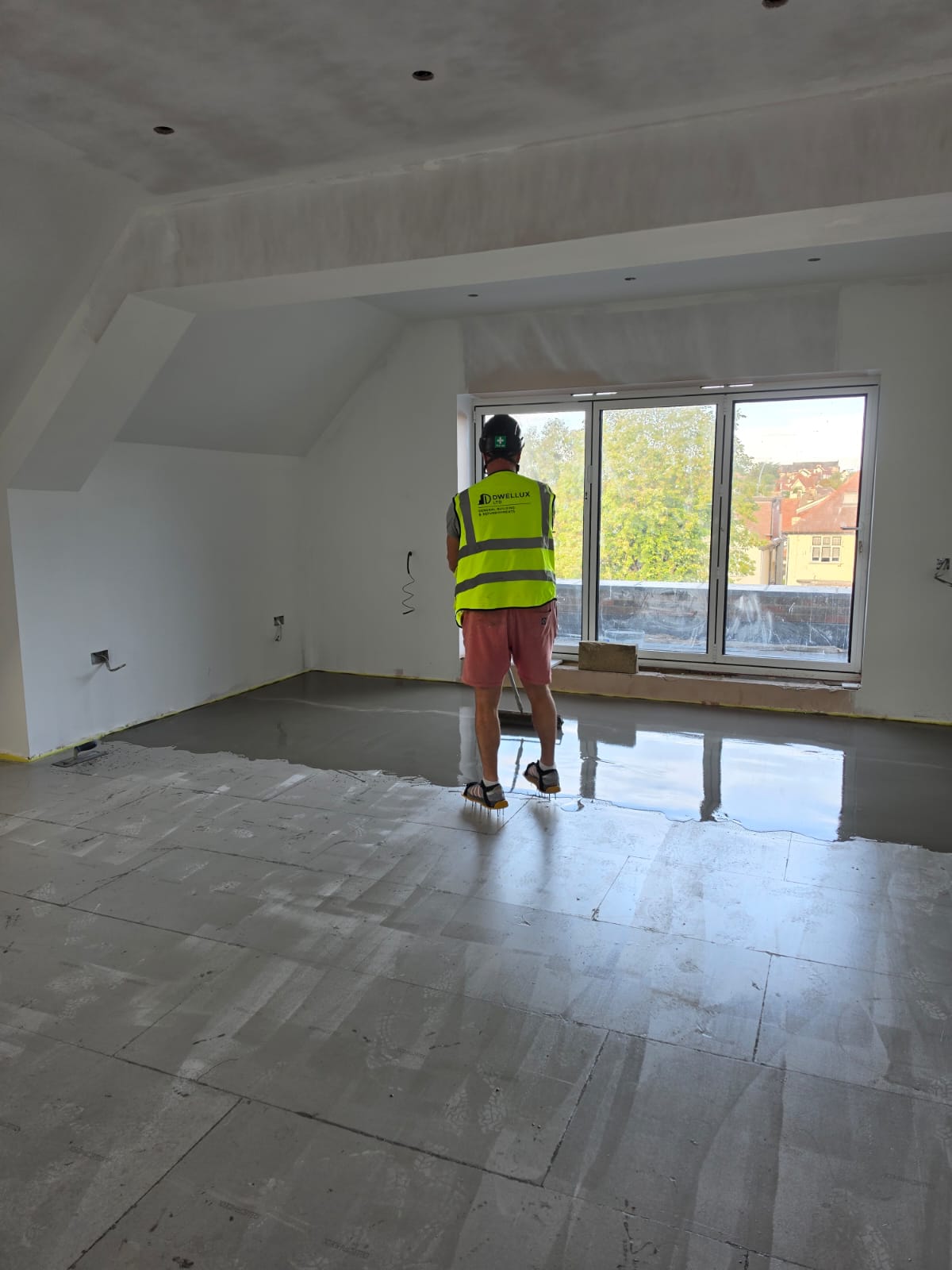 DWELLUX team member in branded hi-vis vest applying self-levelling liquid screed with spiked roller in Southend-on-Sea property