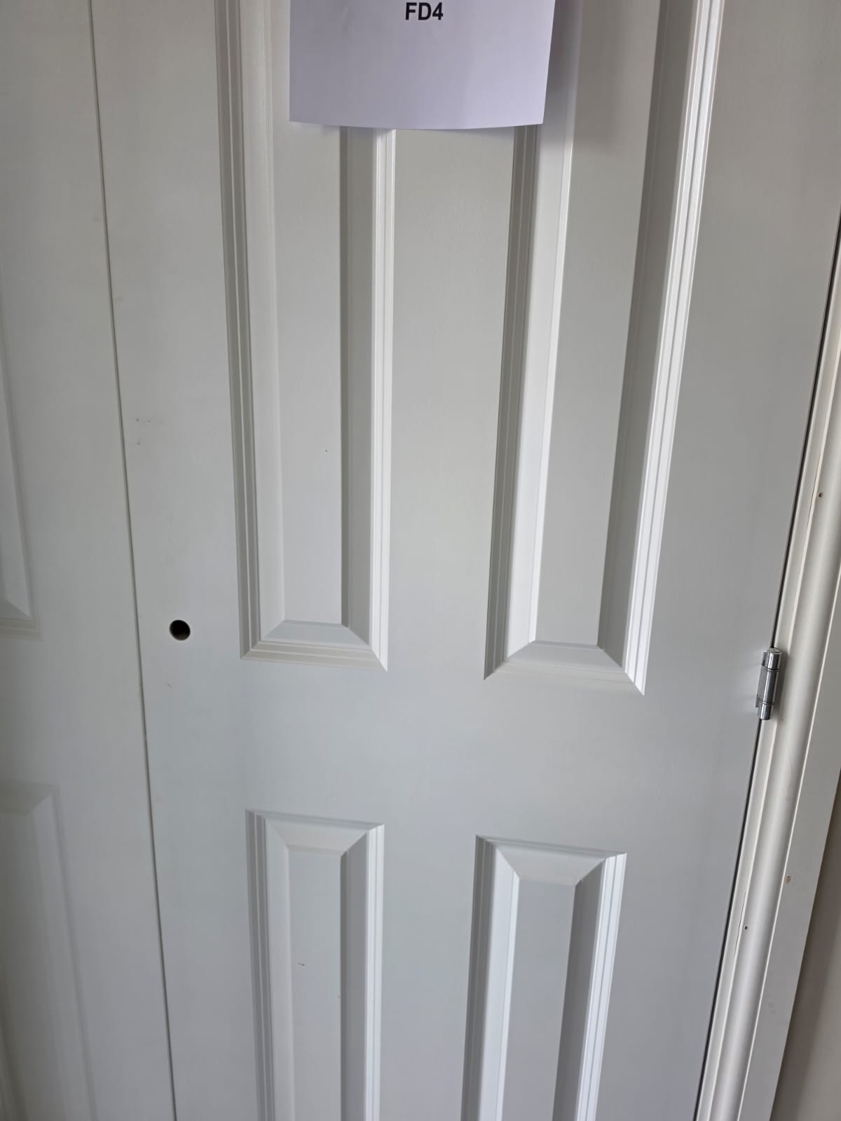 Internal 4-panel fire door FD4 installation and chrome hinge alignment in Harlow residential scheme by DWELLUX