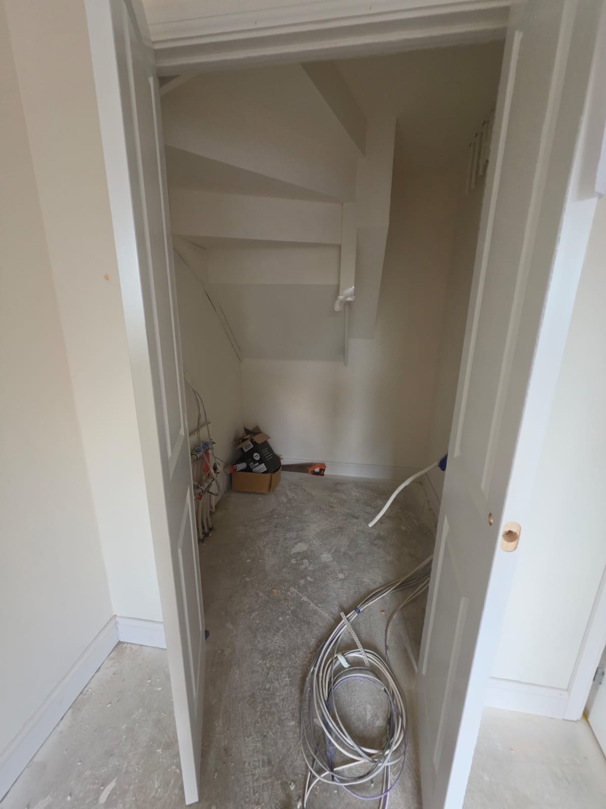 Under-stairs utility store area with underfloor heating manifold and winder staircase carpentry in Harlow by DWELLUX