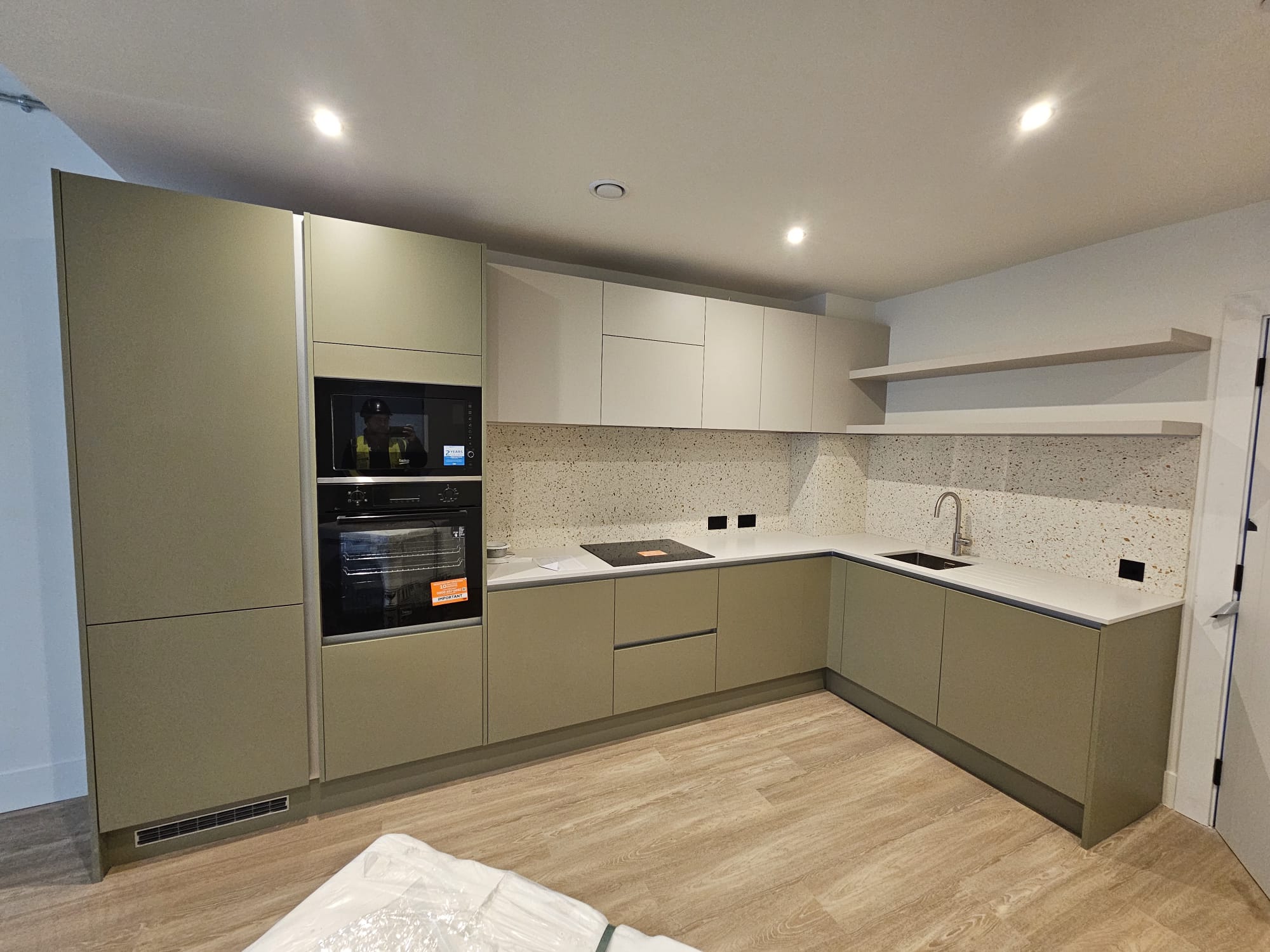 L-shaped sage green handleless kitchen installation with built-in oven, microwave and open shelving in Surrey Quays