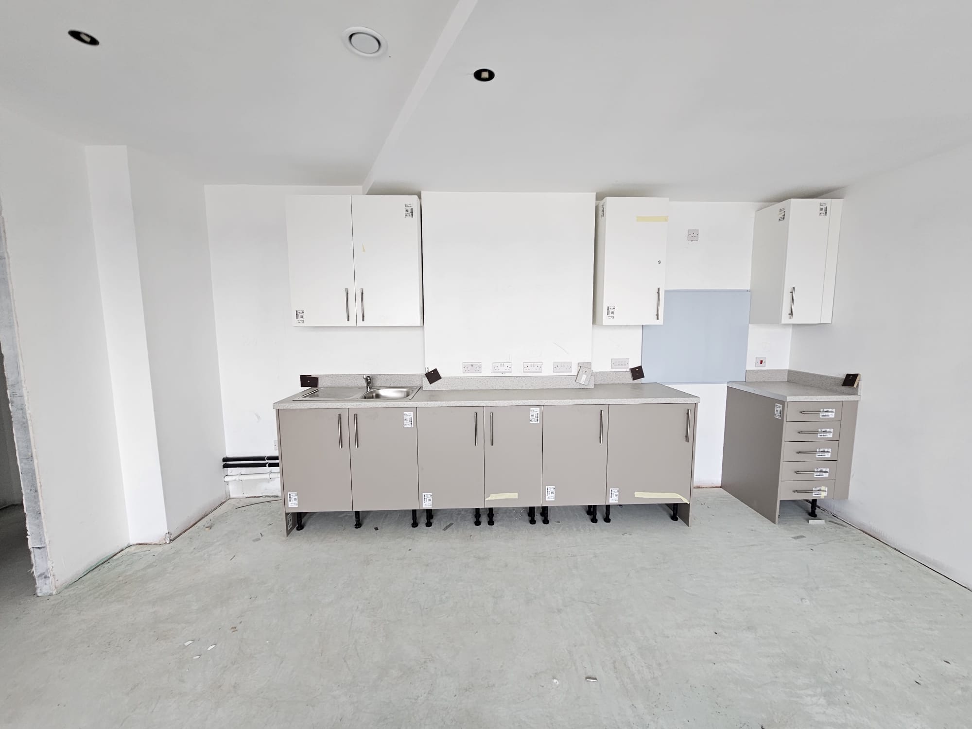 Social housing kitchen unit installation in progress showing base and wall cabinets with protective floor covering in Surrey Quays