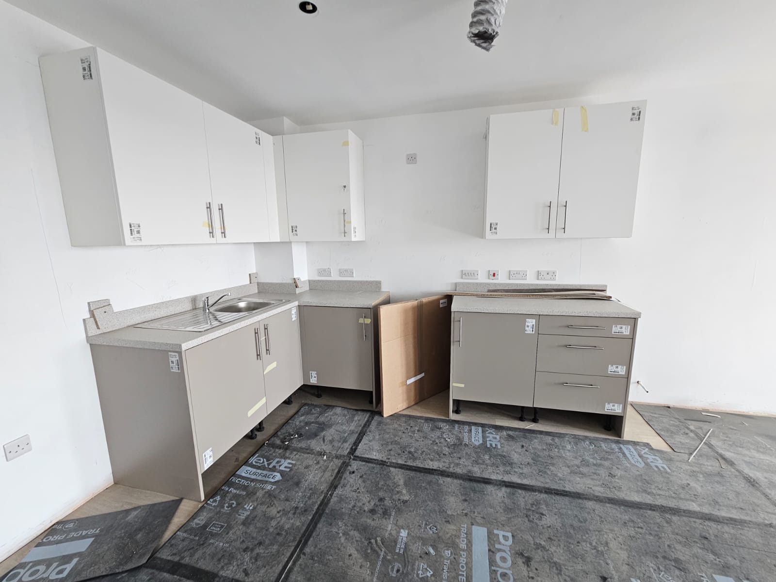 Corner layout kitchen installation during fitting phase with floor protection and unit scribing in Surrey Quays development