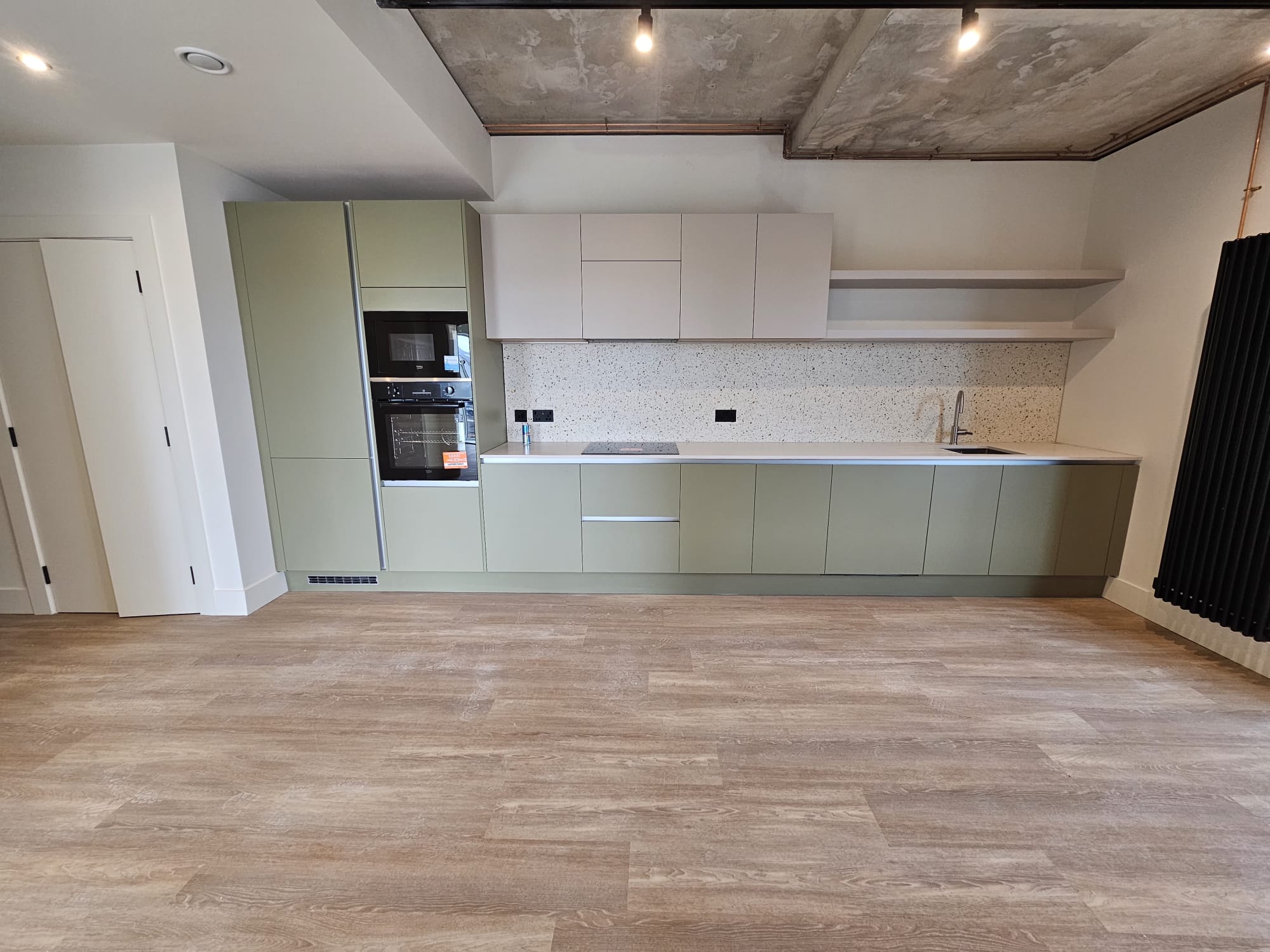 Full room view of completed luxury open-plan kitchen installation with exposed concrete ceiling feature in Surrey Quays