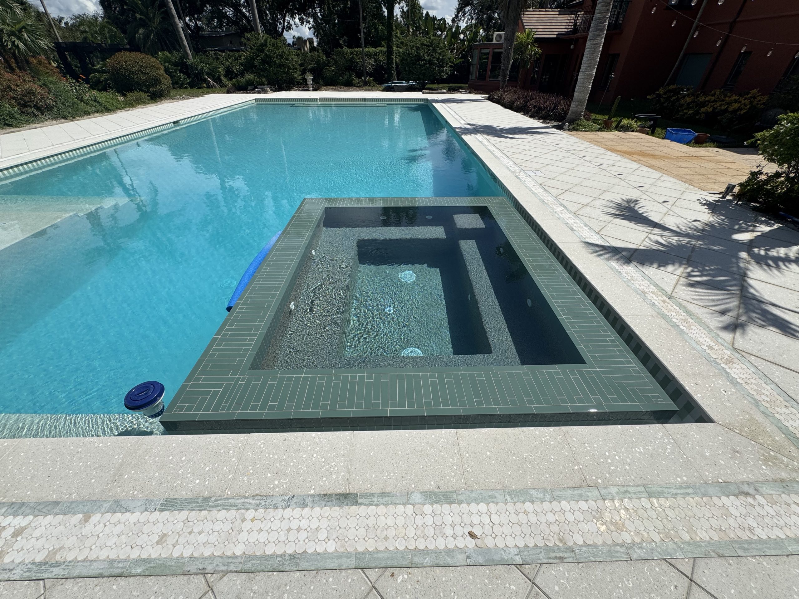 Custom sunken geometric spa with green linear tile rim inside restored historic pool