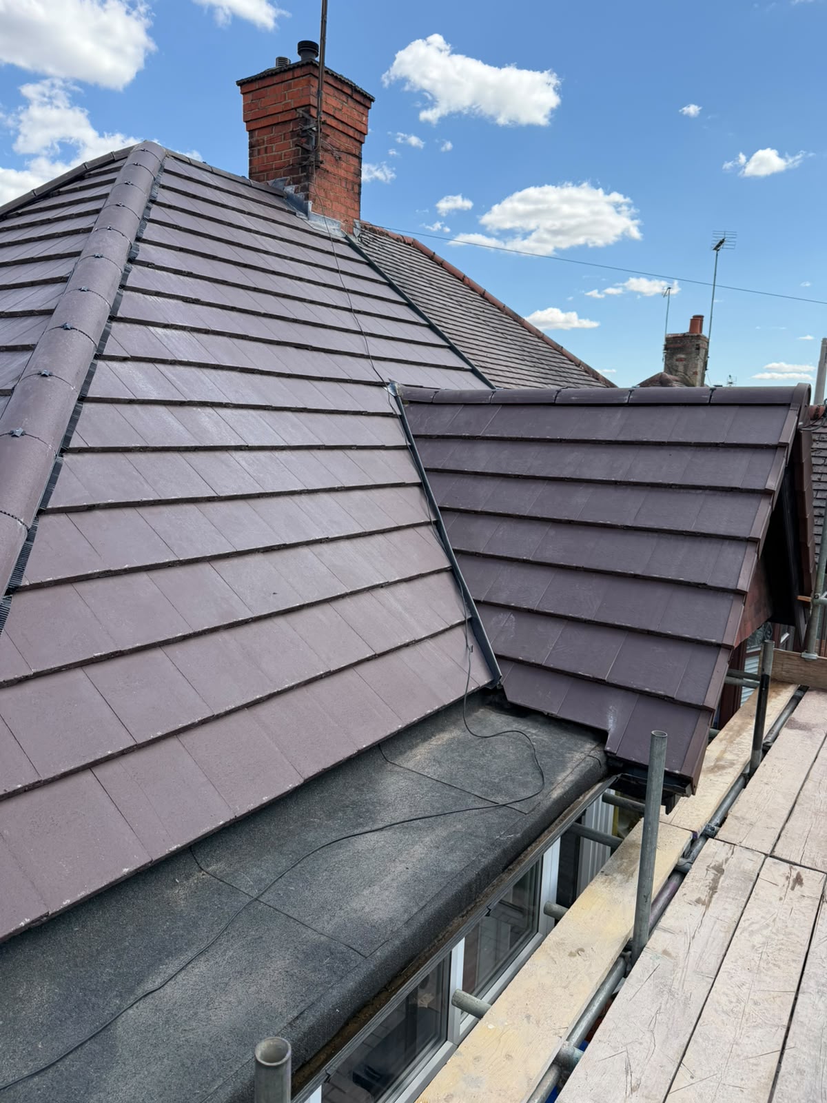 High angle view of completed brown hipped roof, dormer and lead flashing with red chimney stack