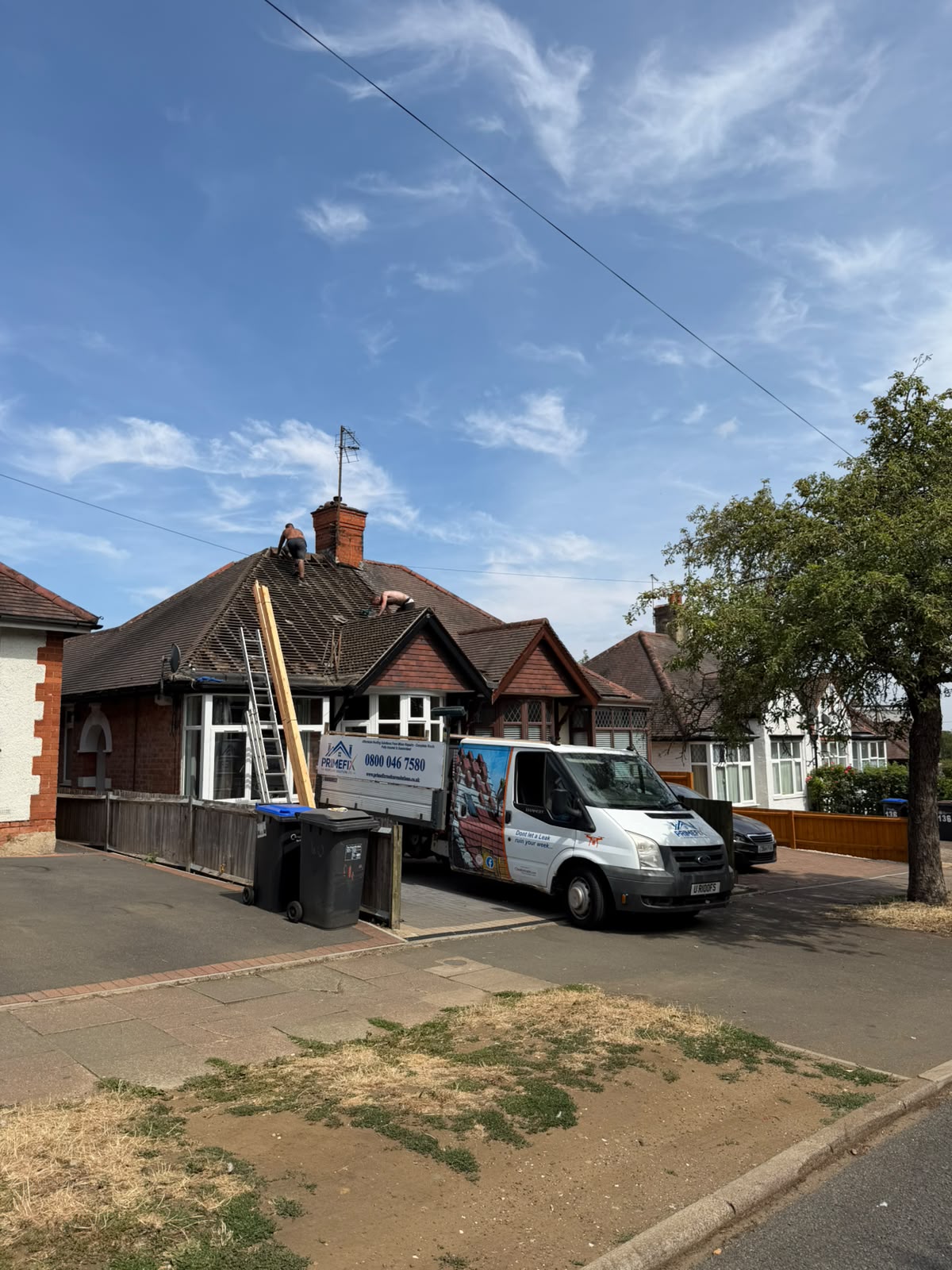 Primefix roofers stripping and preparing bungalow roof covering with company vehicle on driveway