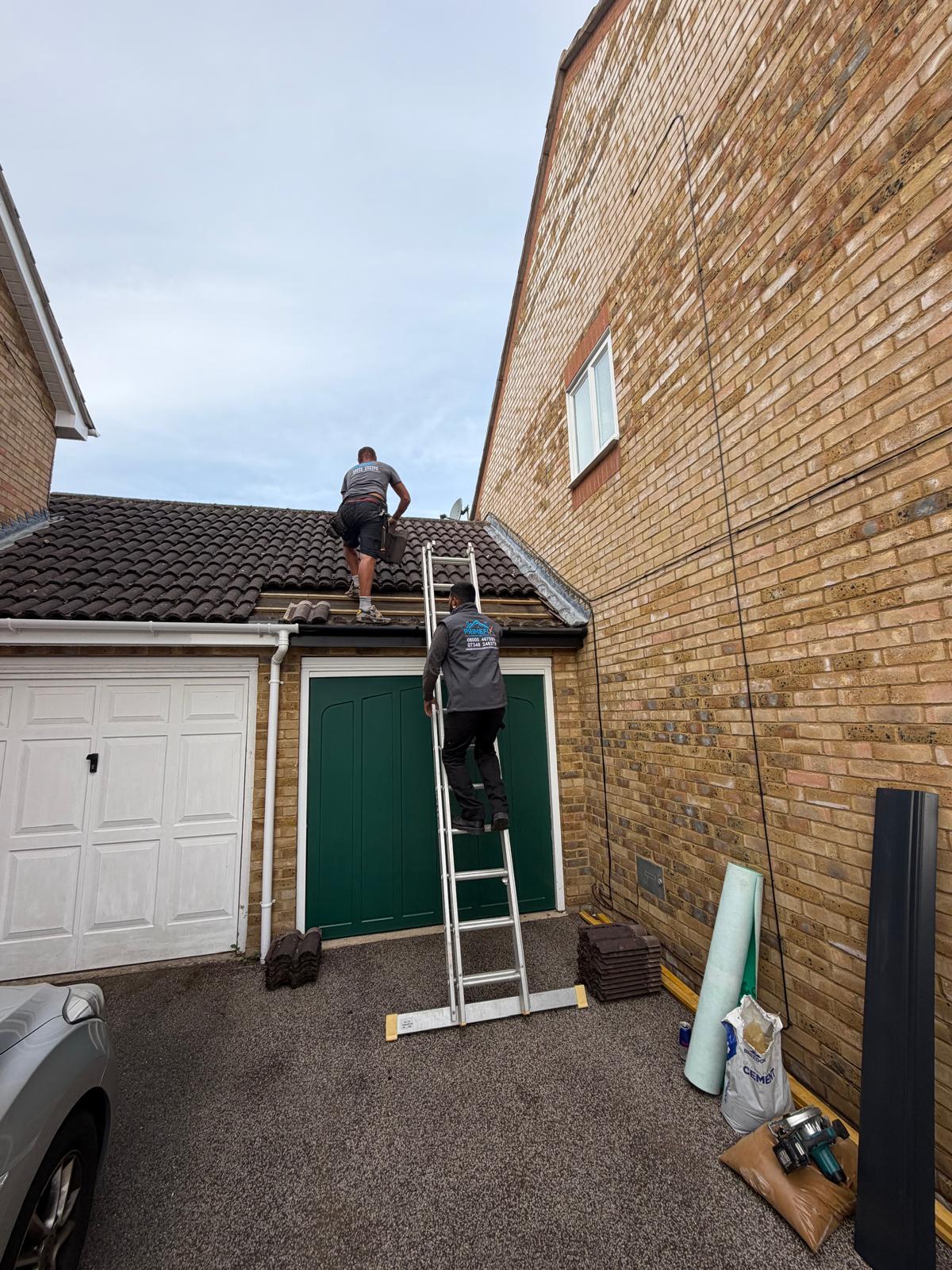 Primefix roofers on ladder carrying out roof tile and batten repairs on garage roof