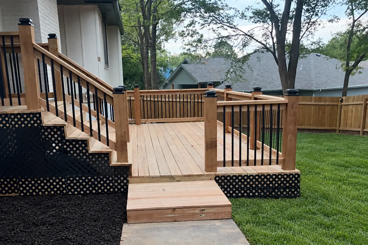 Backyard deck project in Olathe, Kansas, featuring wood decking, black metal railings, stairs, black lattice skirting.