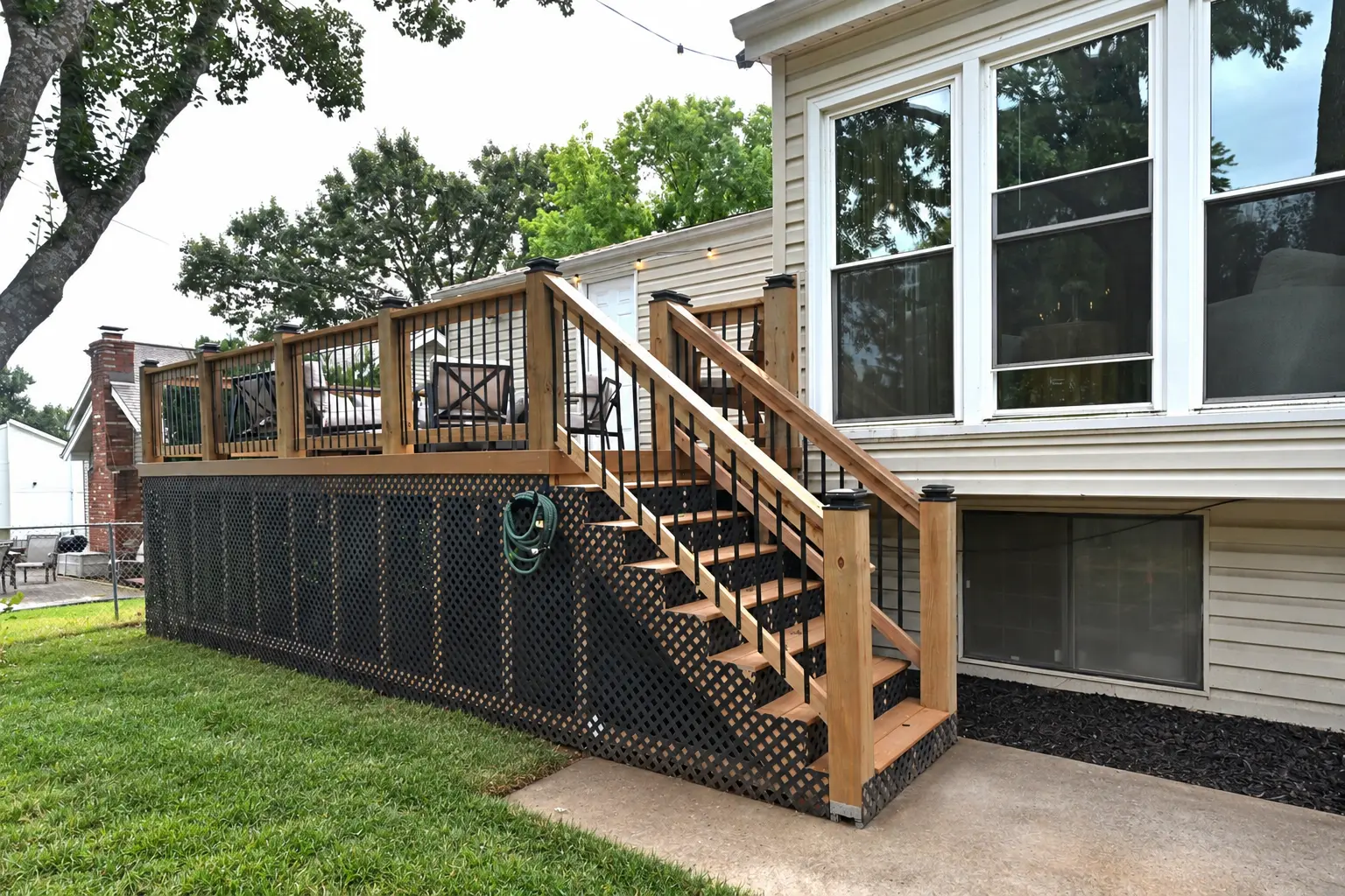 Elevated backyard deck in Lenexa, Kansas, featuring wood railings, black metal balusters, stairs, and lattice skirting.