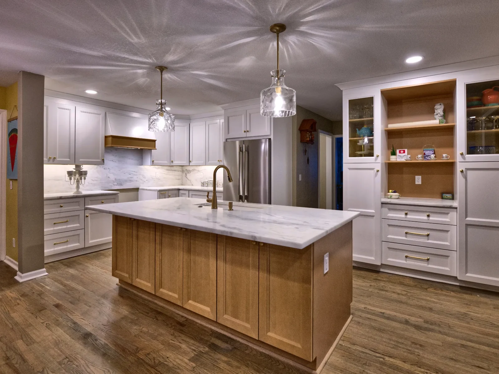 Kitchen remodel in Overland Park, Kansas, featuring white cabinetry, a large center island, pendant lighting, and hardwood flooring.
