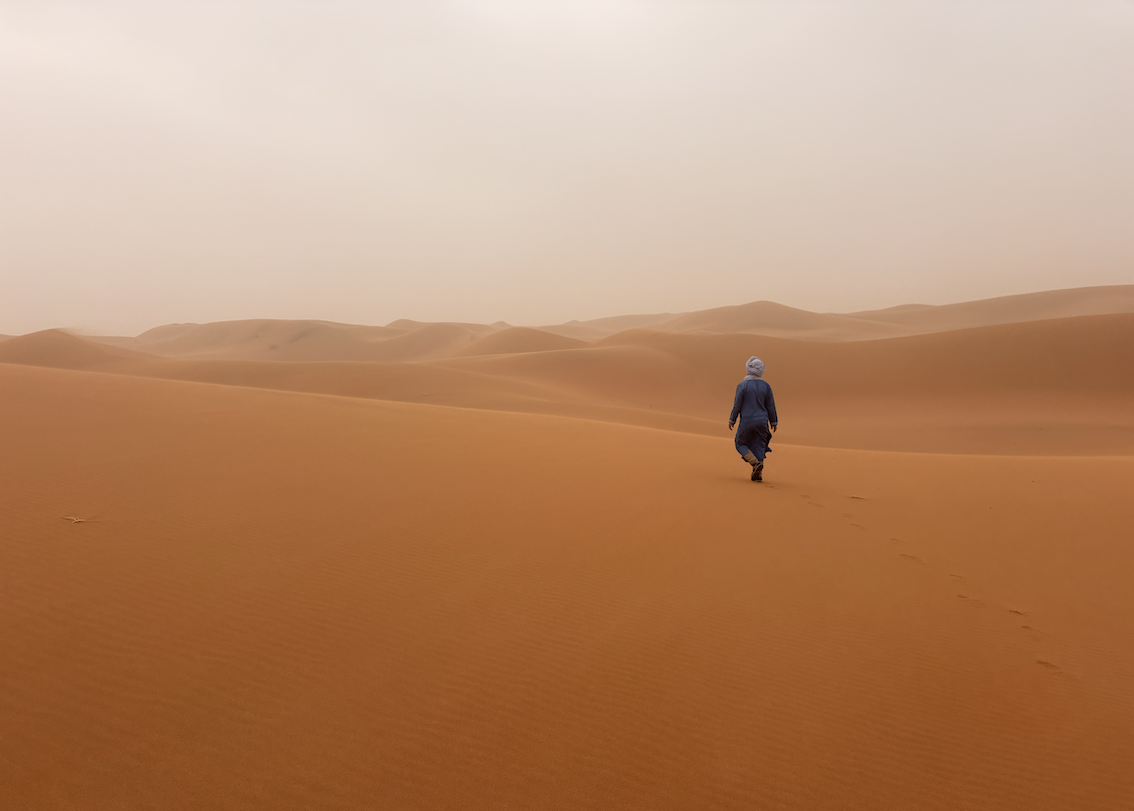 Solitary nomad walking across the quiet Sahara dunes