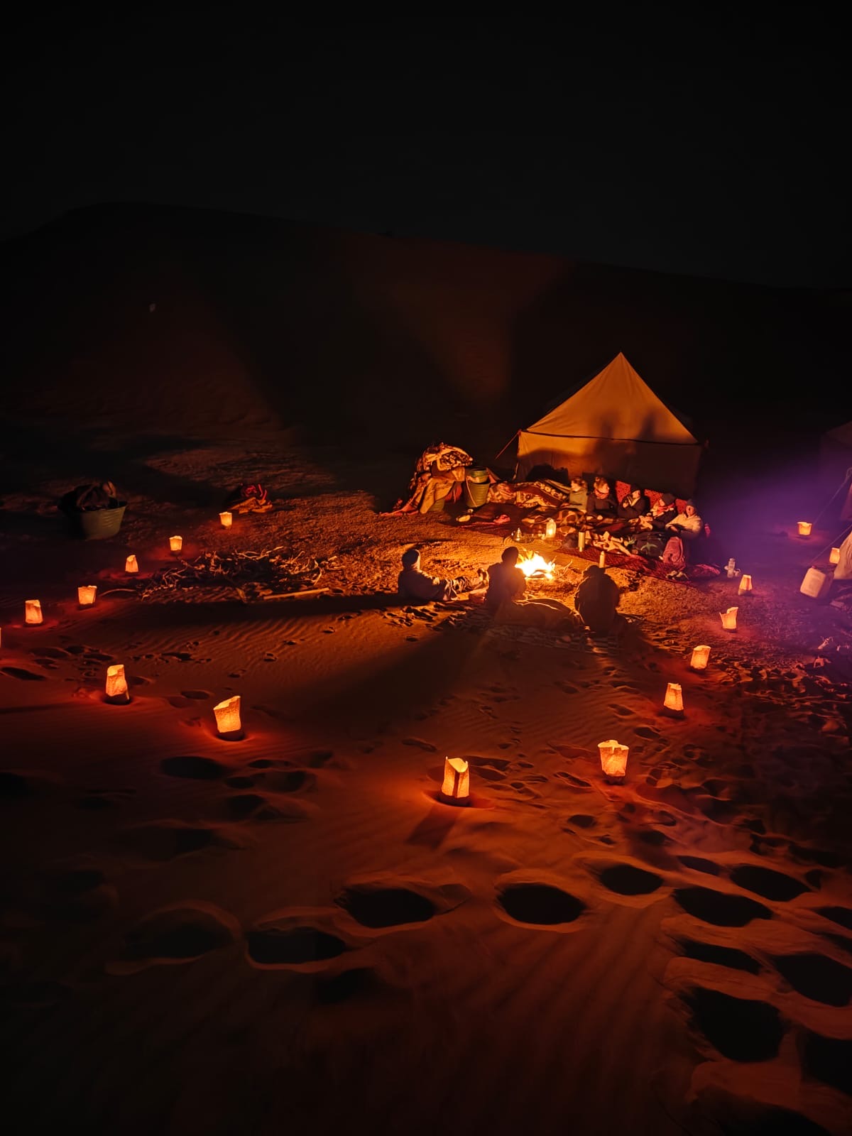 Campfire circle illuminated by lanterns at night in the Sahara dunes