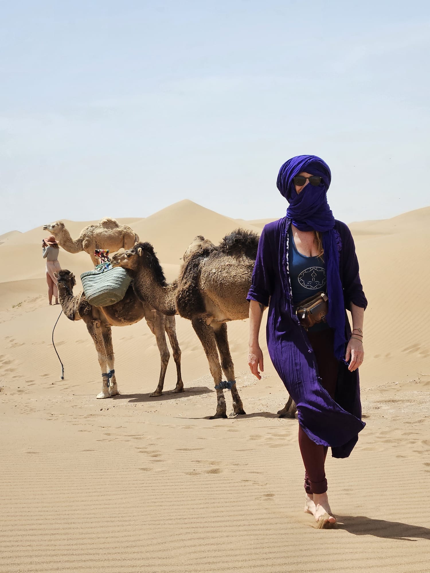 Woman in indigo scarf walking with camels in the Sahara