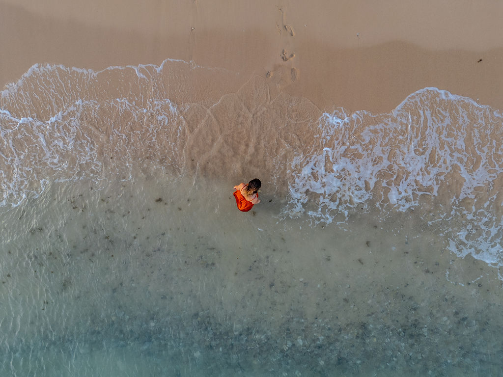 Aerial view of waves washing over sand with woman in terracotta dress