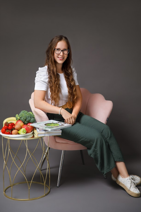 Lengyel-Ortó Eszter dietetikus rózsaszín székben ülve, könyvekkel és gyümölcsökkel