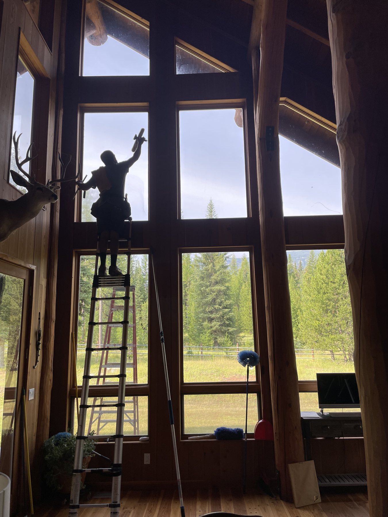 Abraham on a ladder cleaning tall windows inside a log home