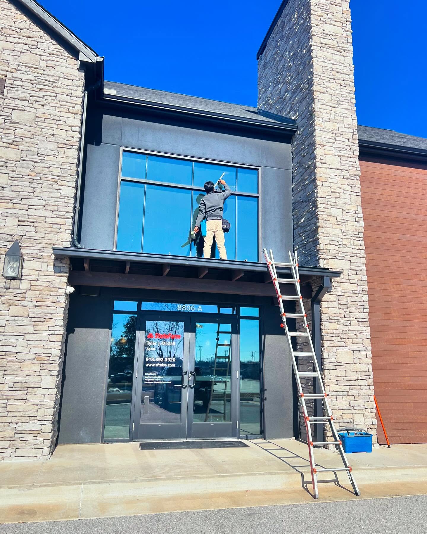 Technician on ladder cleaning storefront windows
