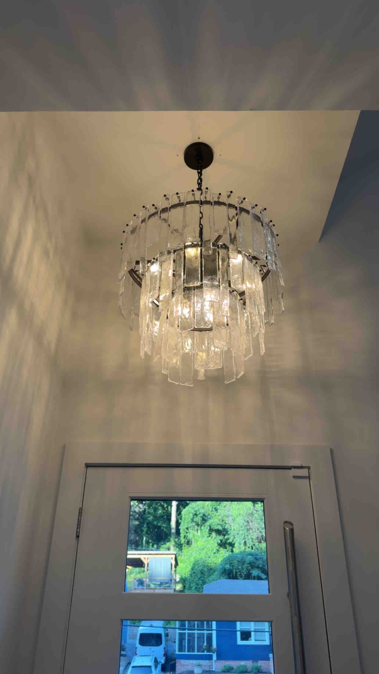 Multi-tier textured glass panel pendant chandelier hanging in a two-story entryway above the front door