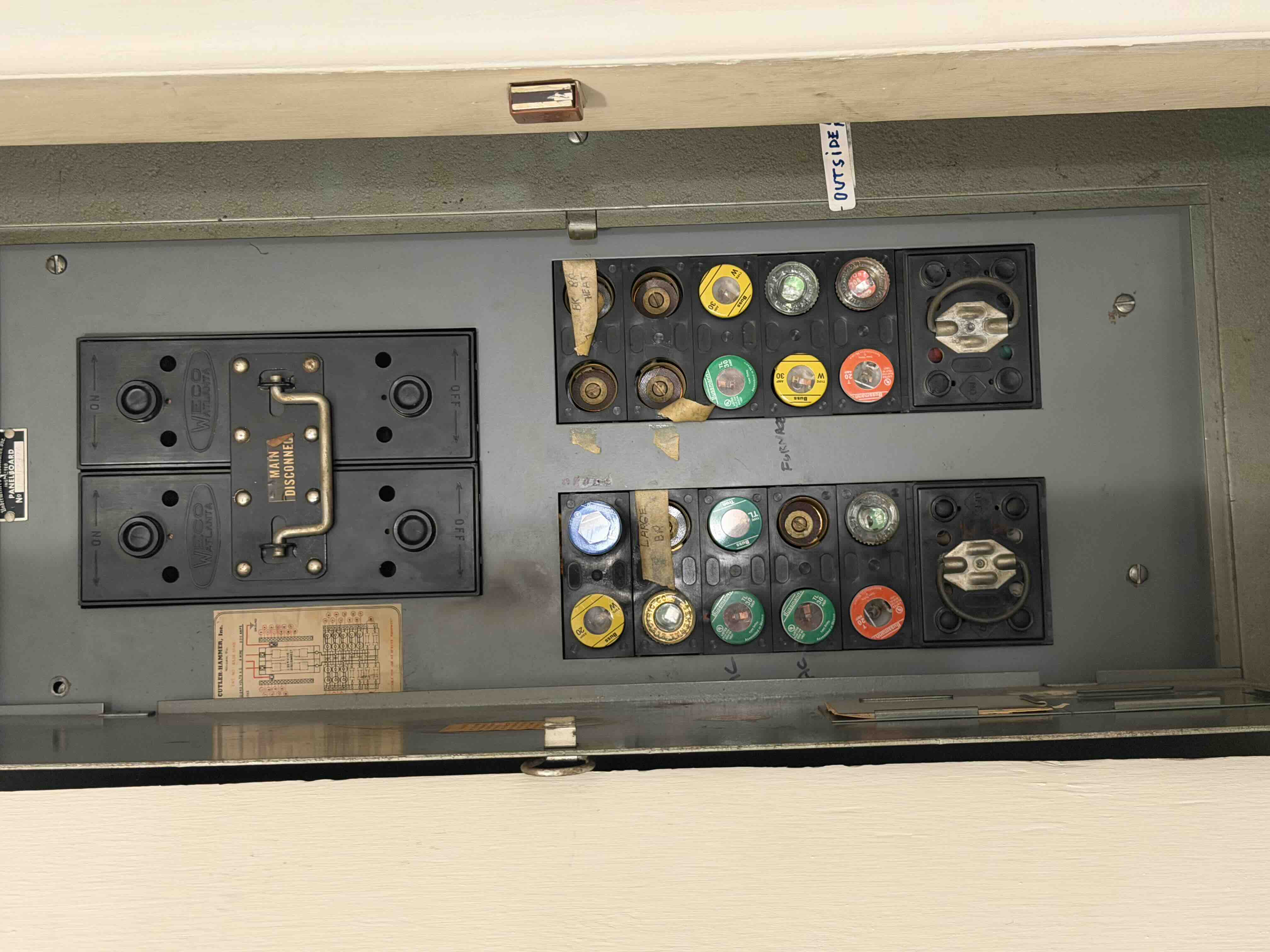 Old fuse panel with a main disconnect handle and screw-in glass fuses before replacement
