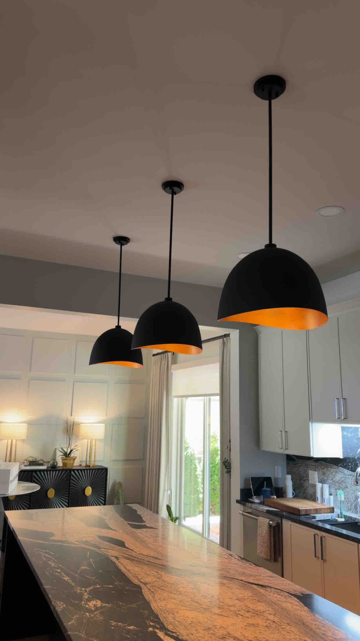 Trio of matte black dome pendant lights with warm gold interior lining over a marble kitchen island