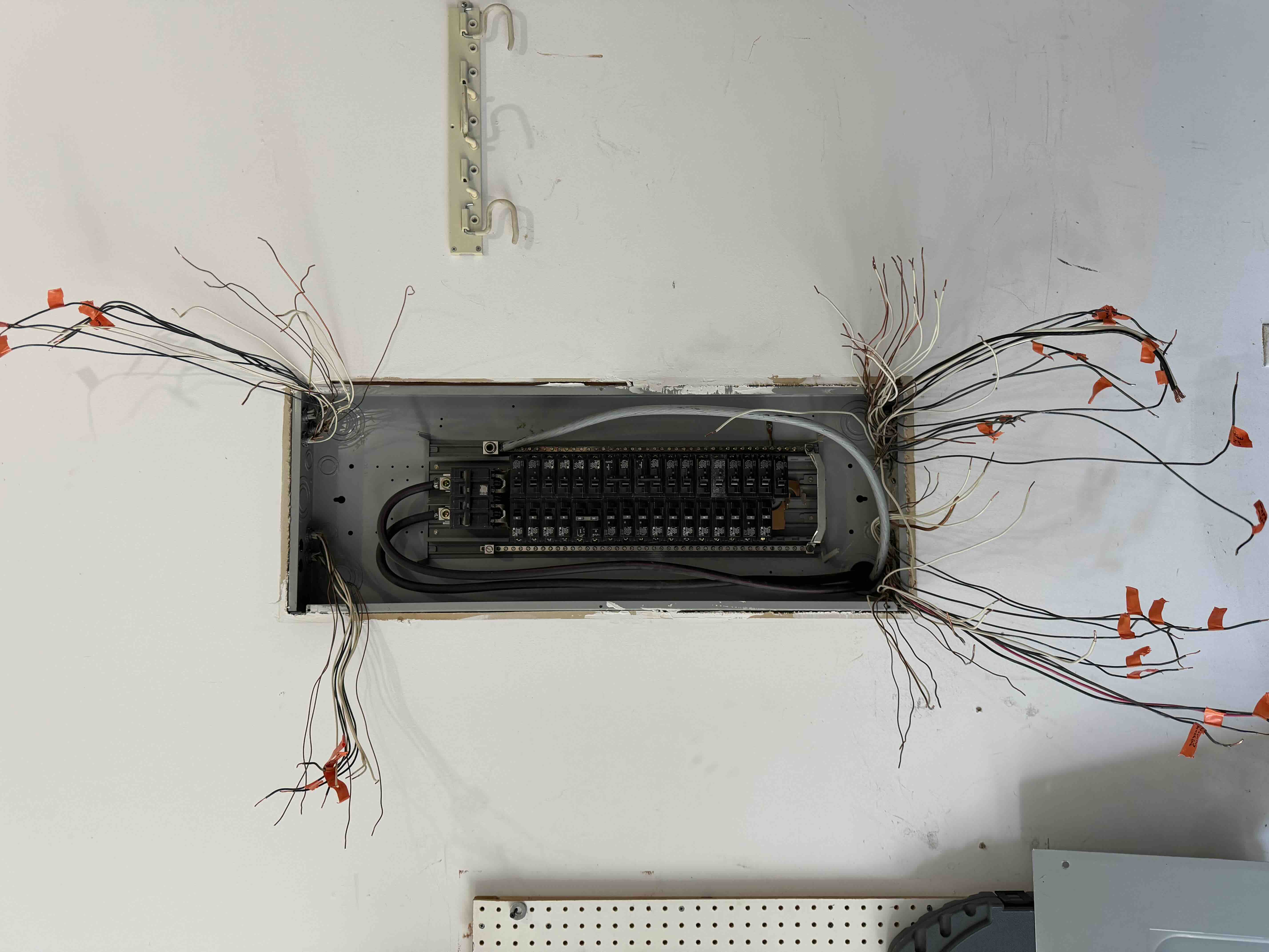New breaker panel box mounted in a wall cutout with circuit wires from both sides individually tagged in orange during a panel replacement