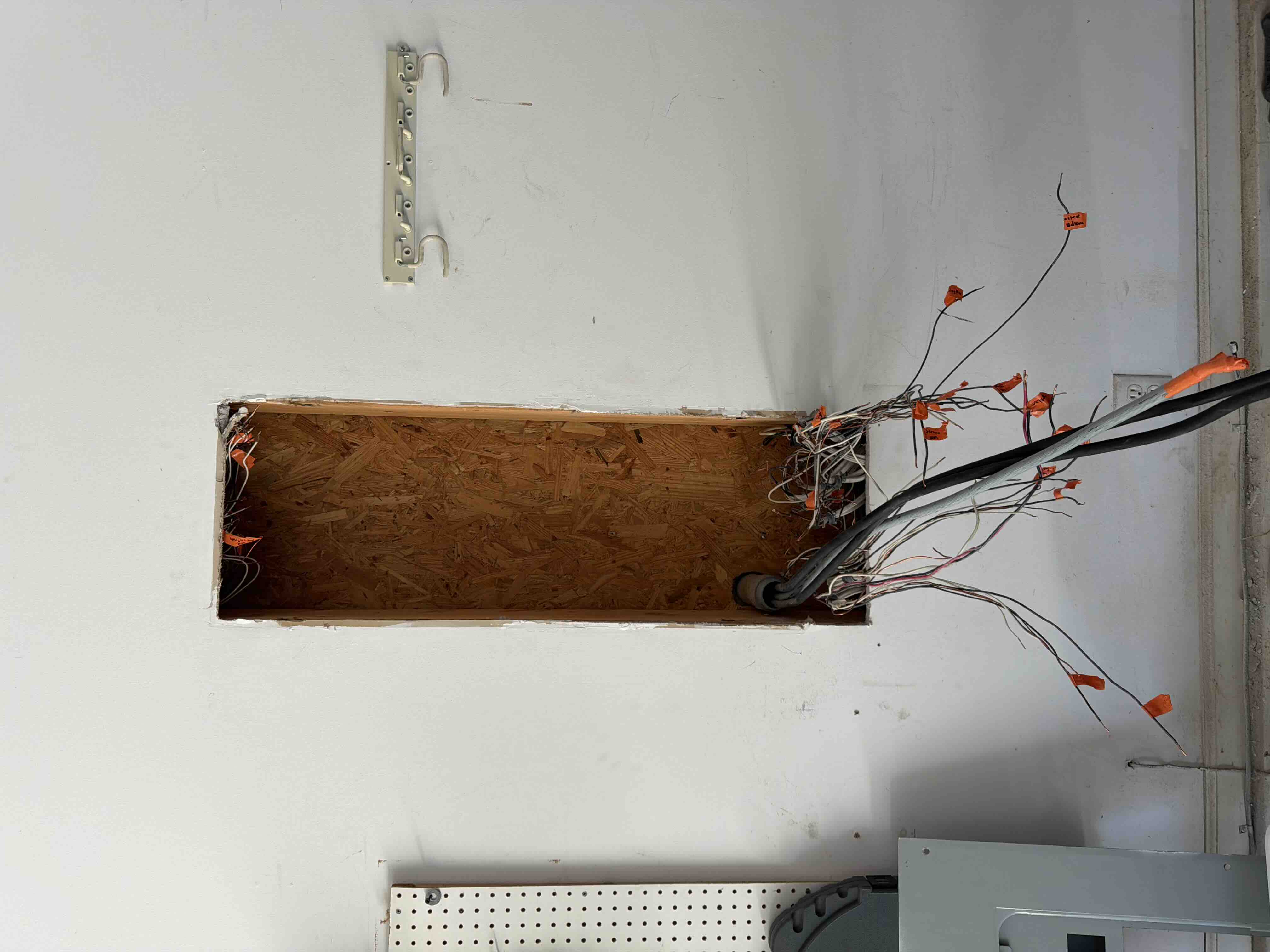 Wall cutout prepared for a breaker panel replacement with bundled circuit wires tagged and set aside before installation