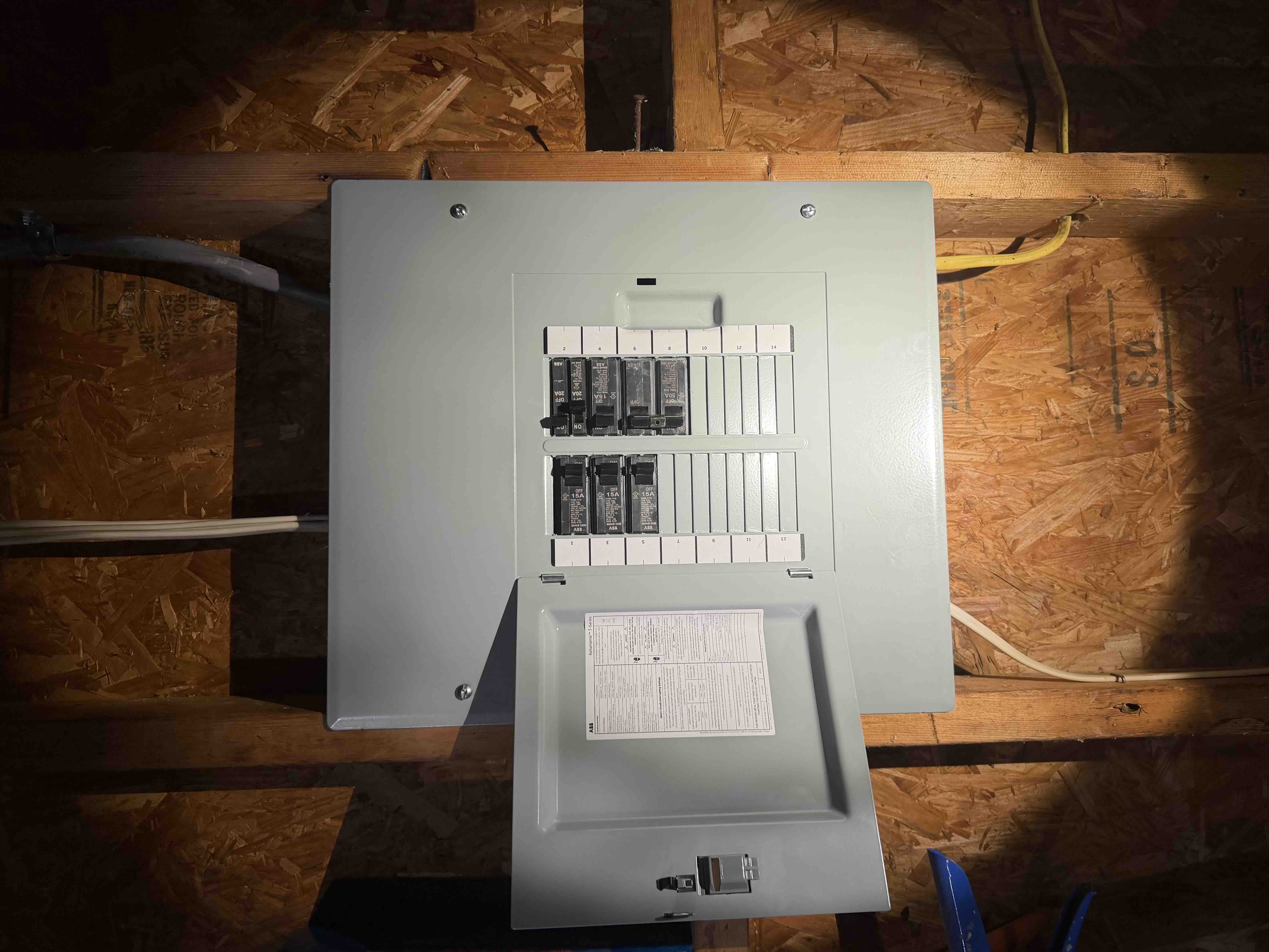 Newly installed ABB load center breaker box mounted in wood framing with breakers and door open