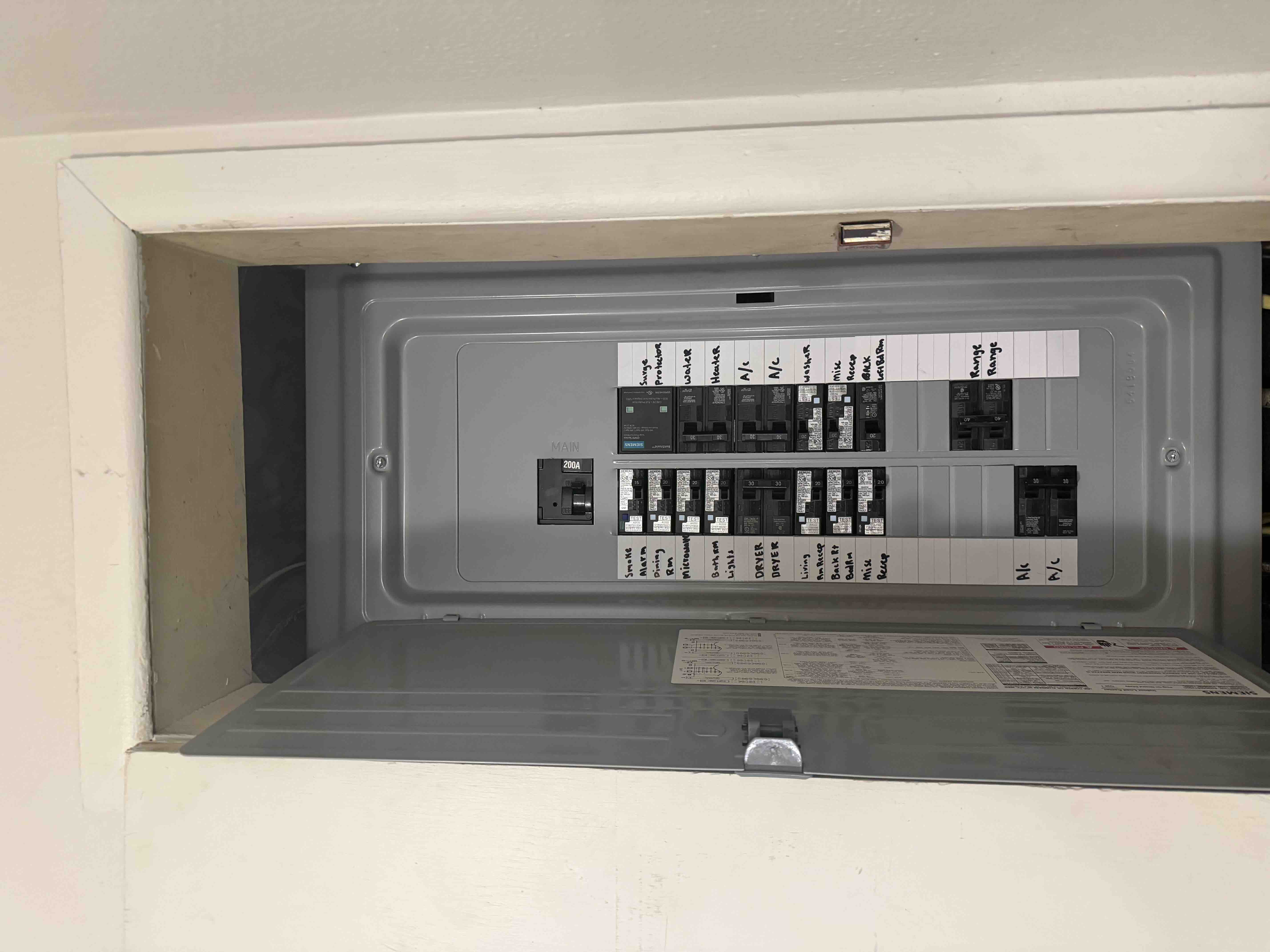 Open 200 amp Siemens breaker panel in a closet with every circuit hand-labeled, including dryer, range, water heater, A/C, and surge protector