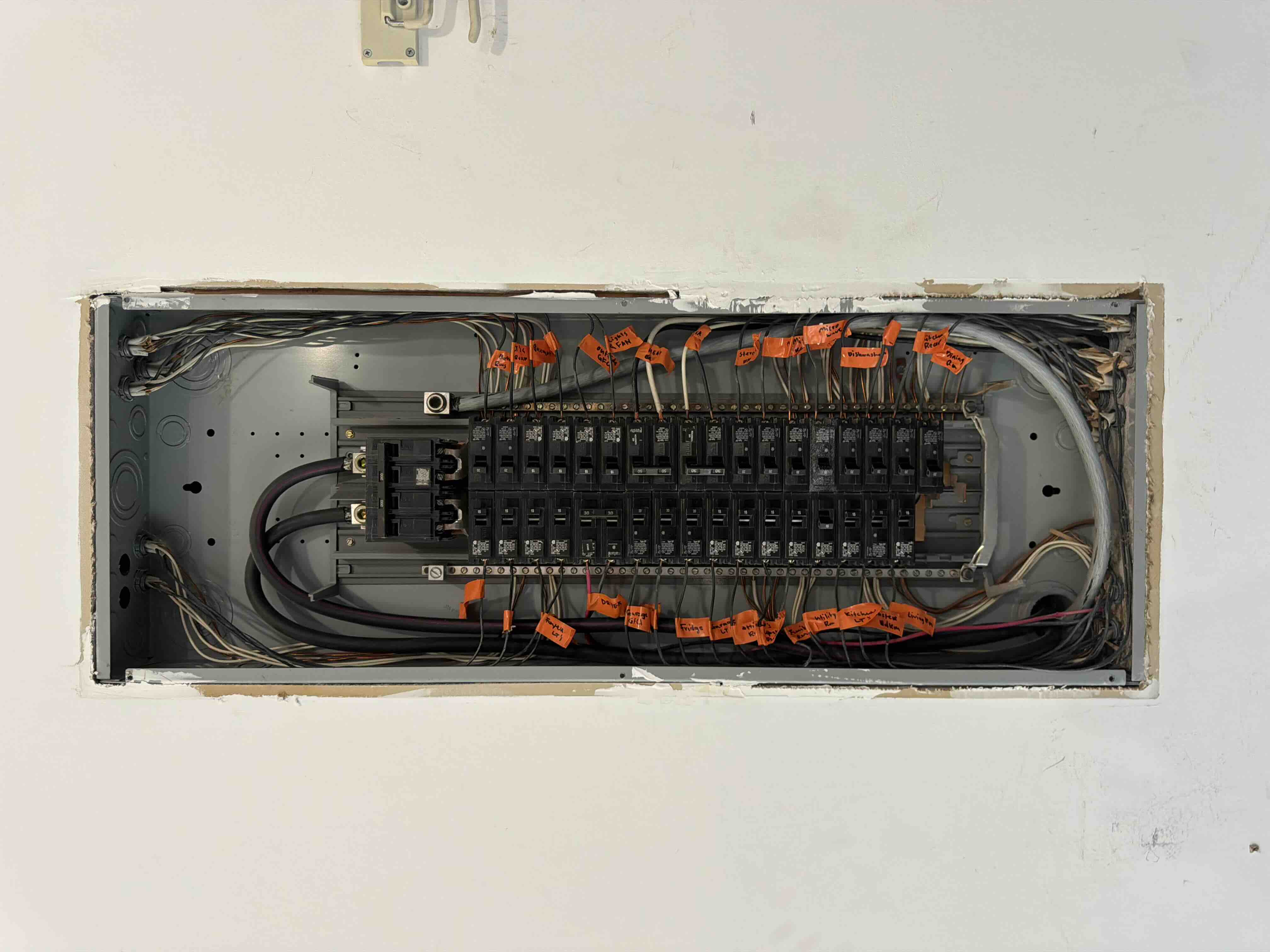 Open breaker panel with circuit wires individually tagged and hand-labeled for rooms such as the kitchen, dryer, and living room