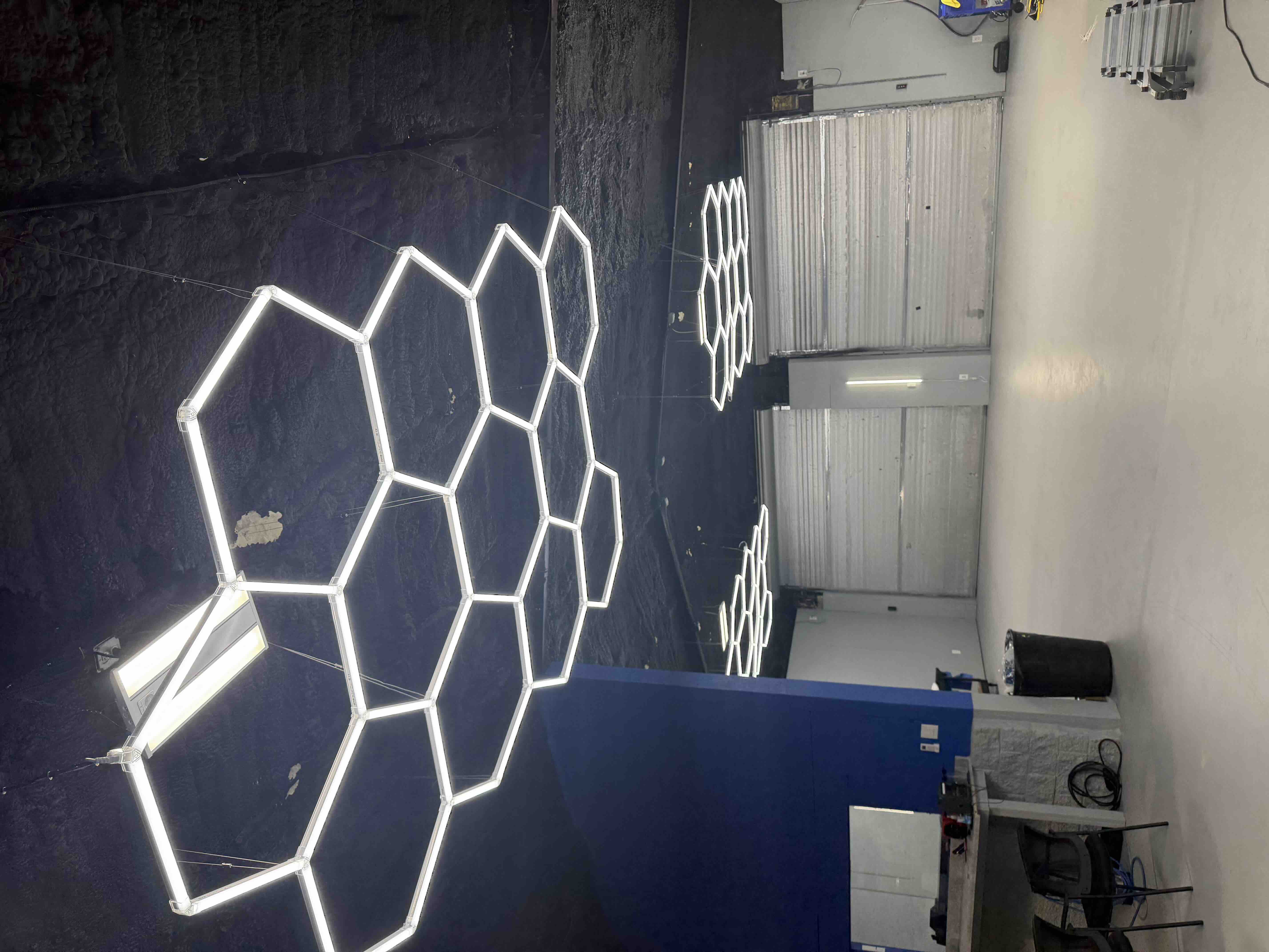 Wide view of multiple hexagon LED honeycomb light fixtures illuminated and suspended in a workshop space