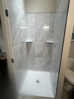 Carrara marble look porcelain shower with frameless glass door and floating shelves installed by Level 4 Tile and Stone