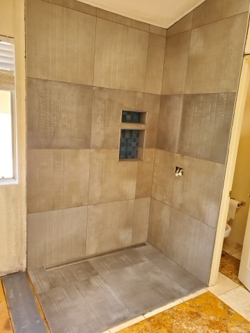 Large format gray porcelain shower with blue glass accent niche by Level 4 Tile and Stone