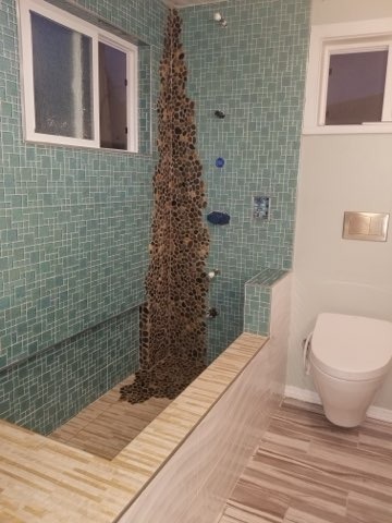 Complete bathroom remodel showcasing teal glass mosaic tile walls and vertical pebble stone feature with wood-look floor tile installation by Level 4 Tile and Stone
