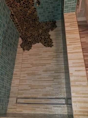Vertical pebble waterfall feature with teal mosaic and wood-look border tiles by Level 4 Tile and Stone San Diego