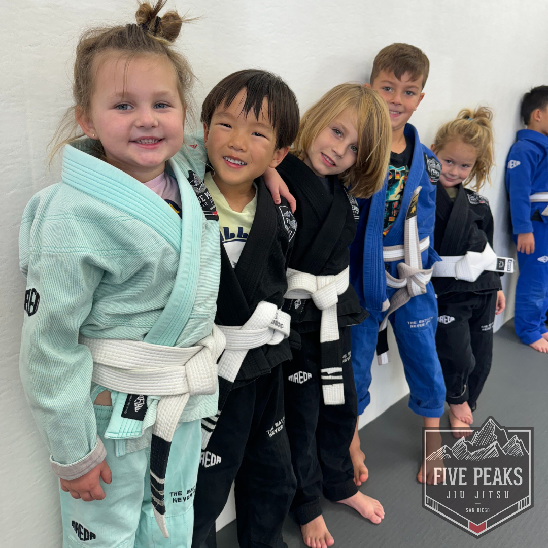 Group of kids in gis smiling together against the wall at Five Peaks Jiu Jitsu