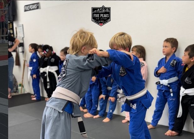 Two young kids practicing jiu jitsu technique together on the mat at Five Peaks Jiu Jitsu