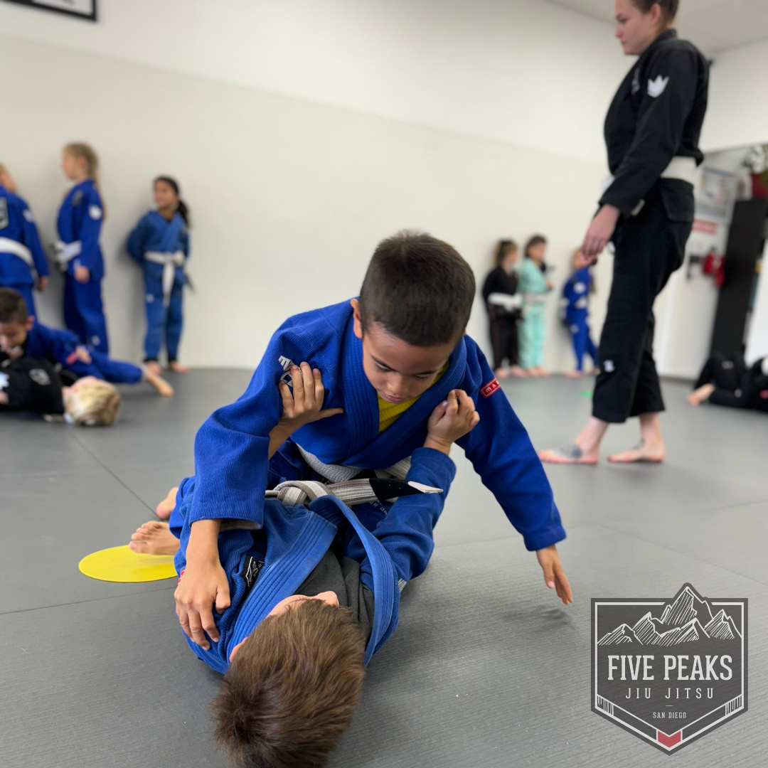 Two kids practicing a jiu jitsu ground technique together on the mat at Five Peaks Jiu Jitsu